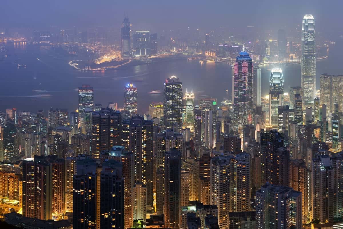 Skyline of Hong Kong at night with illuminated skyscrapers and Victoria Harbour in the background.