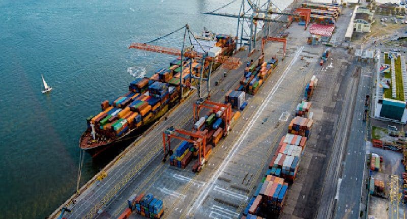 Aerial view of a busy cargo shipping port with colorful containers and cranes by the water.
