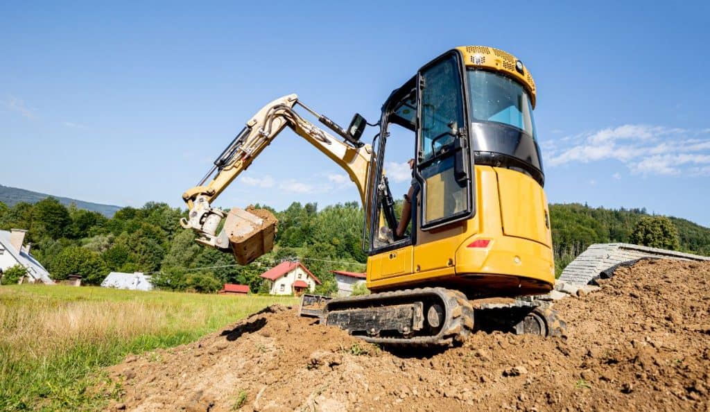 Mini excavator digging in a yard near a row of houses
