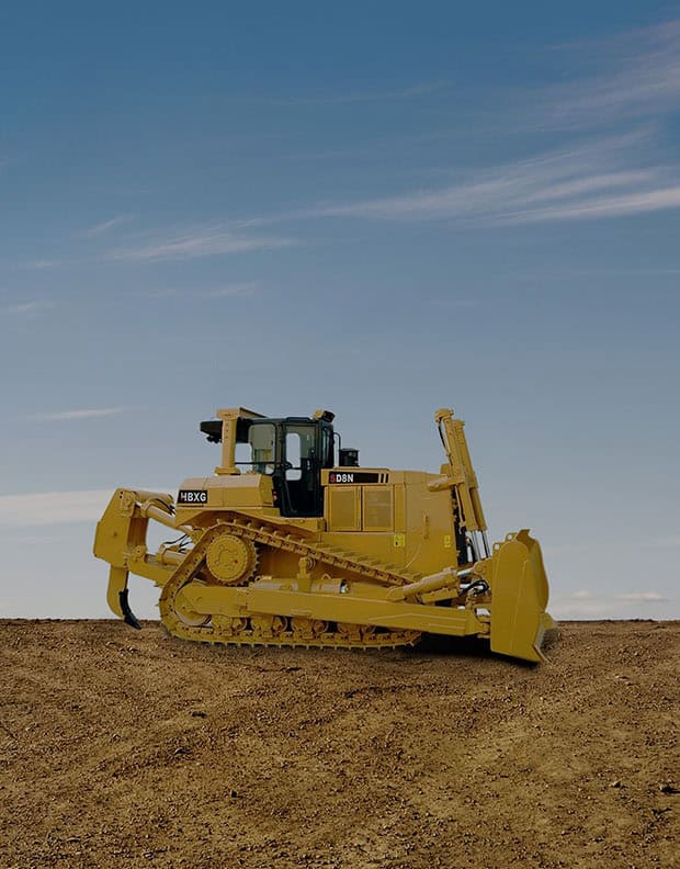 Yellow bulldozer on dirt, clear blue sky in the background.