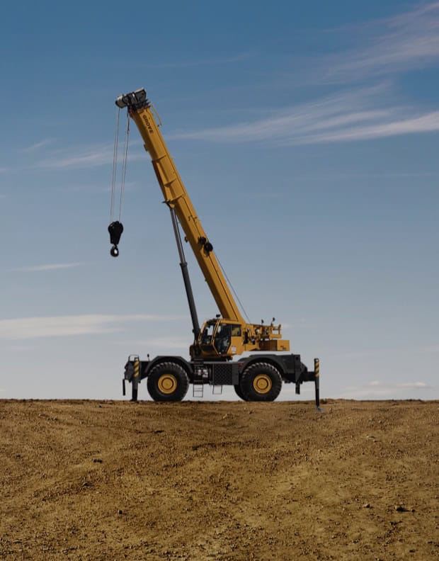 Large yellow construction crane on dirt road under blue sky.