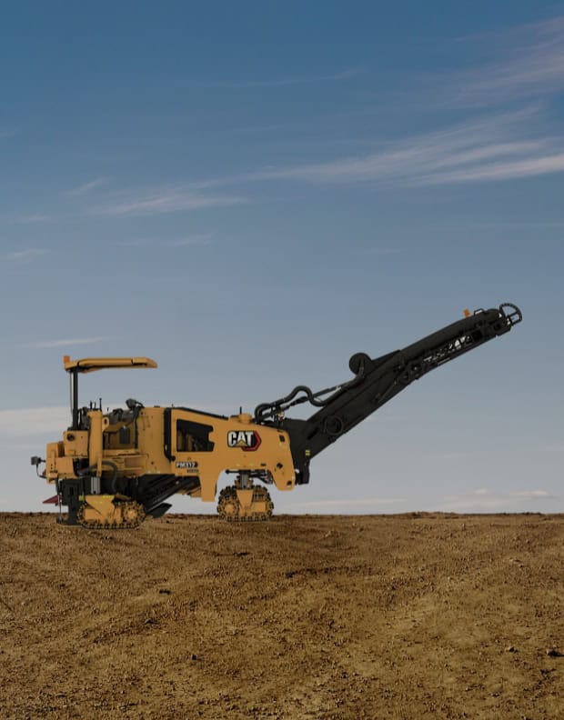 Yellow Caterpillar PM622 cold planer machine on a dirt construction site under a clear blue sky.