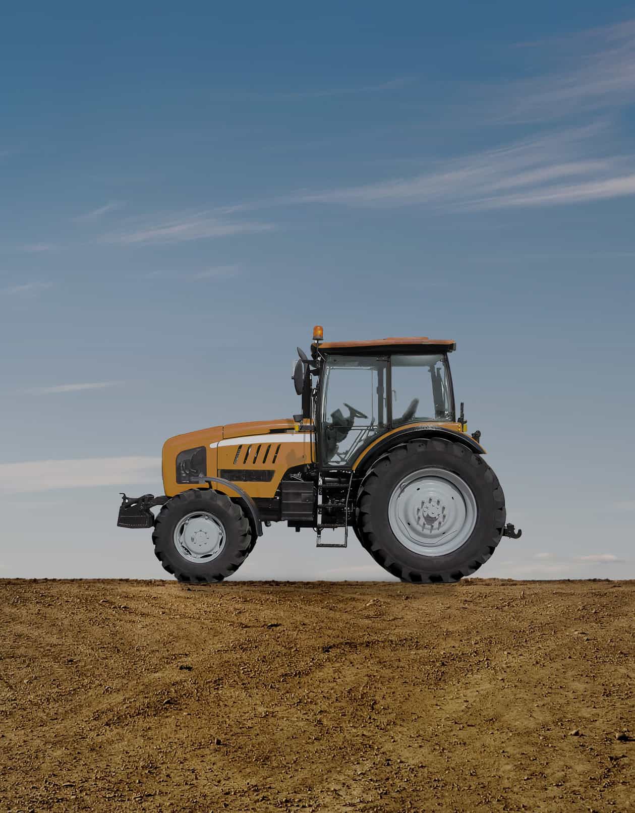 Yellow tractor on a dirt field under a clear blue sky.