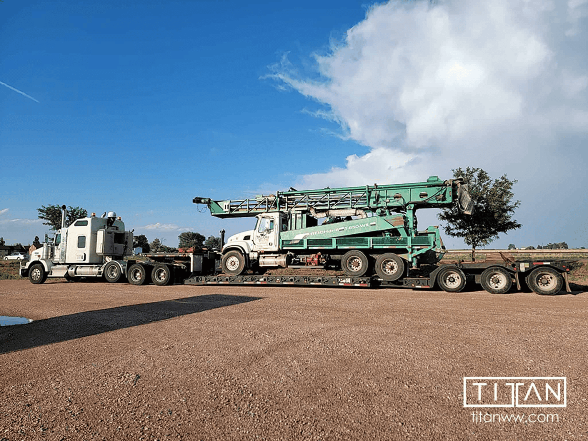 White semi-truck transporting green drilling rig on lowboy