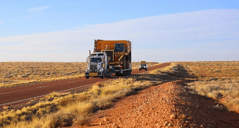 Oversized truck hauling yellow excavator.