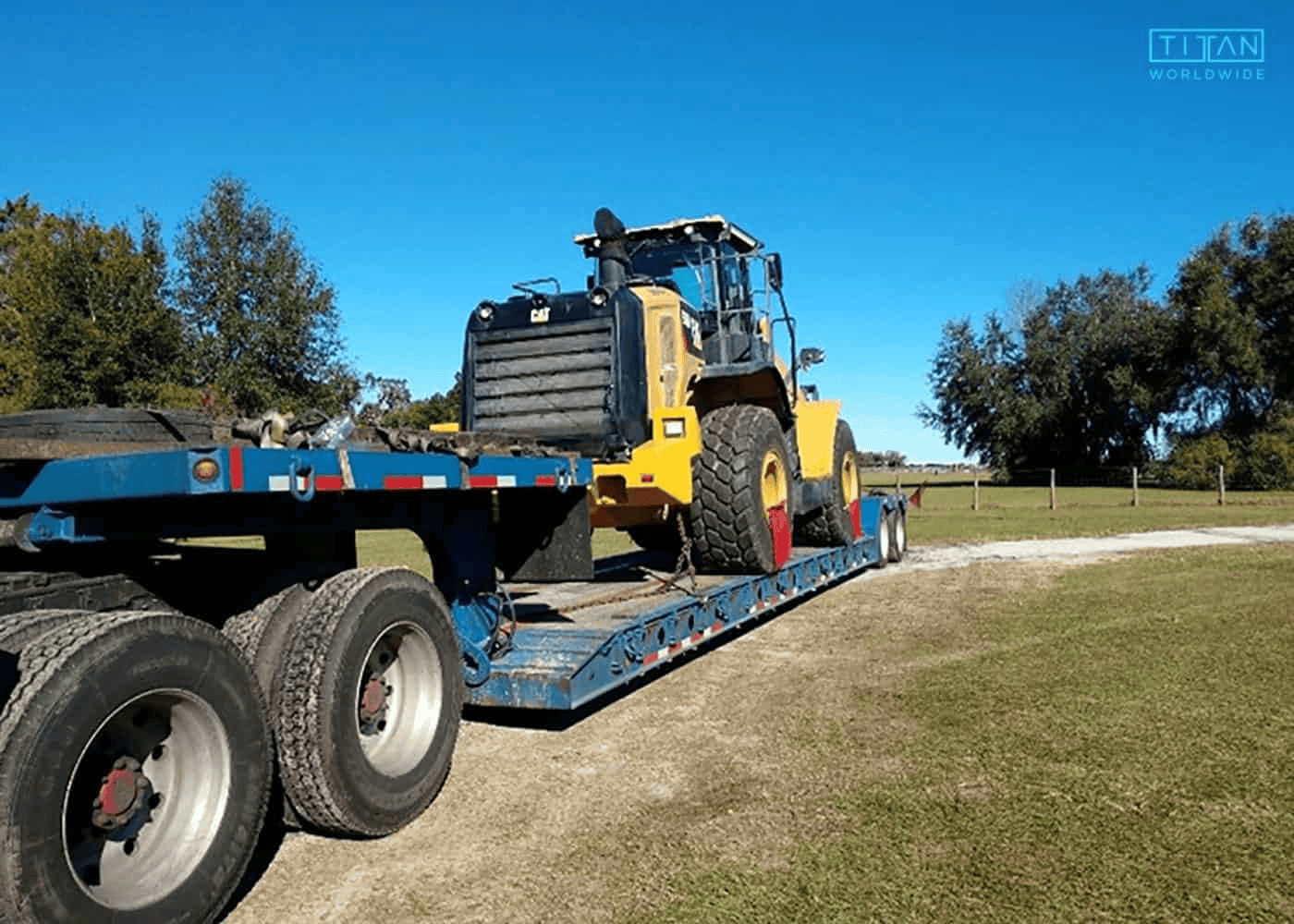 Yellow wheel loader on blue flatbed trailer outside.
