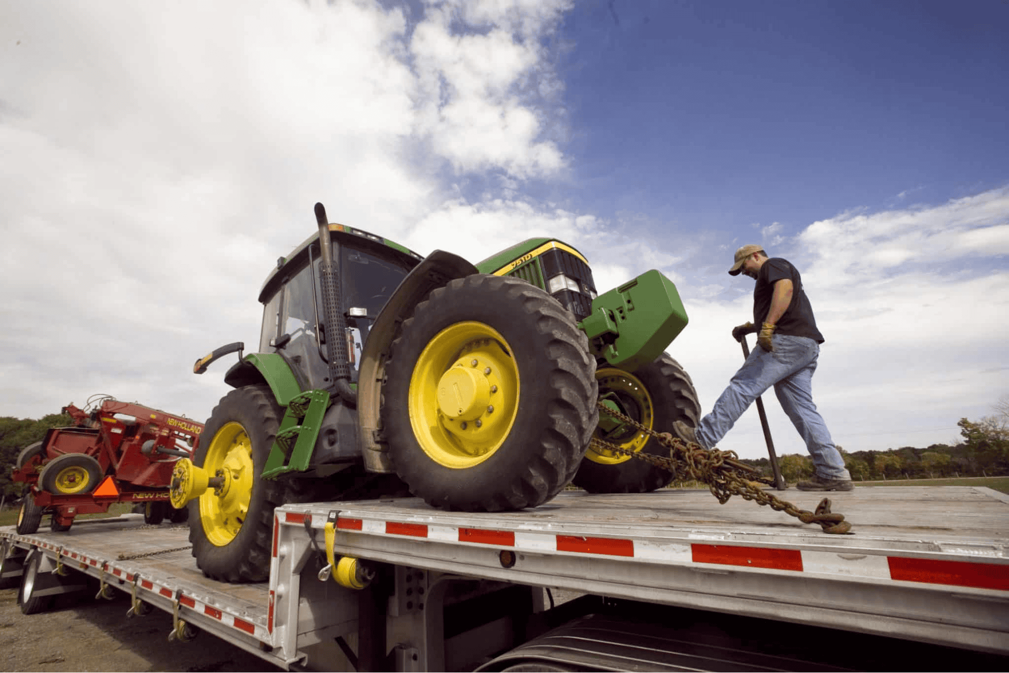 Worker securing John Deere tractor on flatbed trailer.