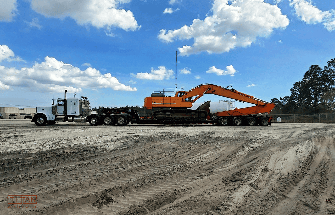 White truck hauling orange excavator on flatbed trailer.