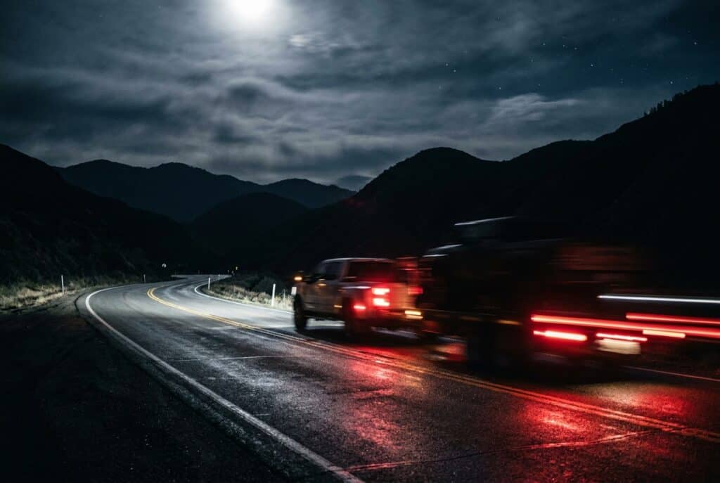 Oilfield trucking vehicle on road with passing cars illuminated by moonlight.
